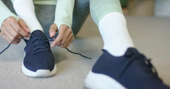 African American woman sitting on carpet reaching loose navy shoelace and tying bow for secure fit
