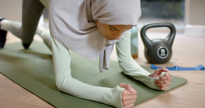 Female in hijab kneeling, placing forearms on mat and lifting into one-leg plank for core strength