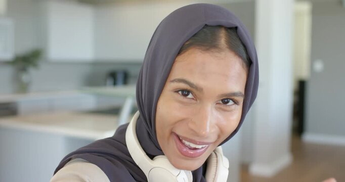 Pressing record for vlog, African American woman in hijab with headset, waving, speaking in kitchen