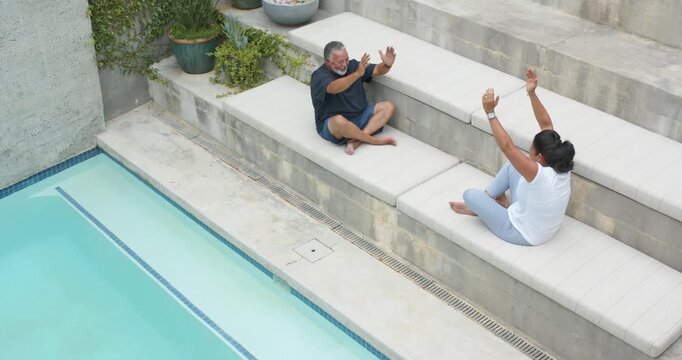 After stretch cue African American couple mirroring raising arms leaning reaching legs resting pool