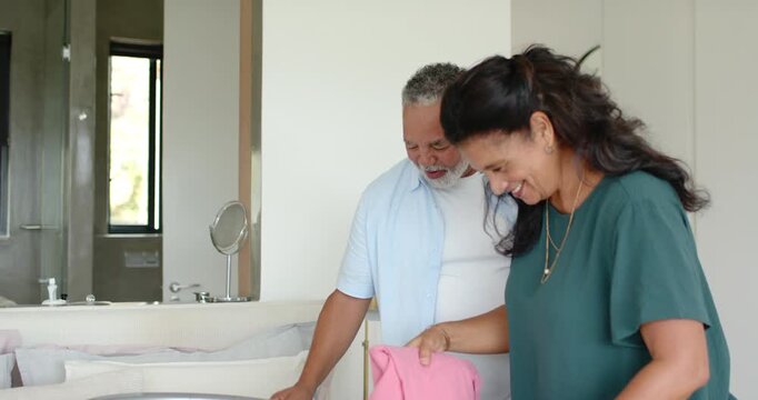 African American couple folding linens at bassinet at home as man holding pink cloth preparing room