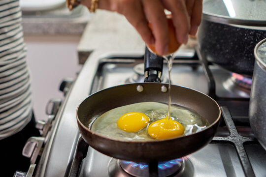 Hands cracking eggs in frying pan for breakfast