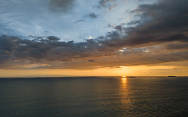 Fototapeta premium Golden sunlight dances on calm ocean waves at sunset over distant islands