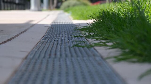 Linear drainage grate along a paved pathway beside a sports field in Australia with grass edging. Urban infrastructure, water runoff management, surface drainage, and maintenance design