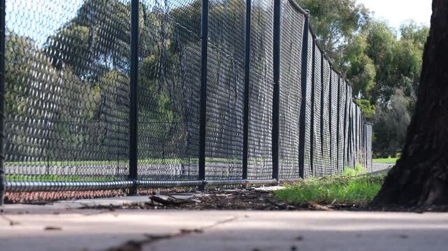 Low-angle view along a chain-link fence bordering a baseball or softball field in Melbourne, Australia. Sports ground infrastructure highlighting boundary fencing, community recreational facilities