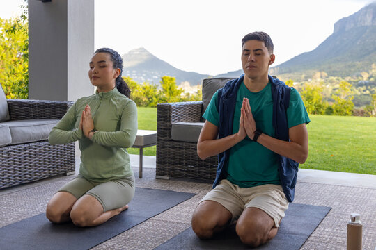 Couple kneeling on covered patio yoga mats in activewear, pressing hands, wrist tracker visible