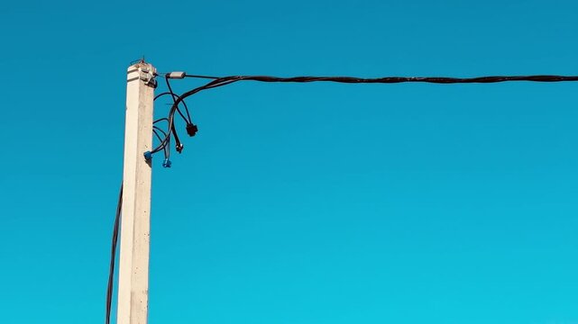 Concrete pole with electric wires sky clear blue background, slender concrete column supporting overhead cable, curved drop wire.