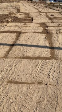 Temporary concrete slab road covered mud, sunlit construction corridor with deep tire tracks, sand packed joints between slabs.