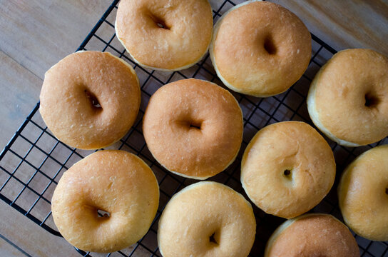 A dozen freshly baked golden donuts cooling on a wire rack over a wooden table. High-angle wide shot of a large batch of homemade doughnuts for a family breakfast or bakery.