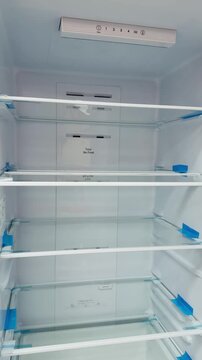 Empty refrigerator interior with glass shelves, pristine white cavity, overhead LED illumination, adjustable glass racks with blue