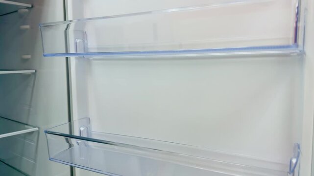 Empty white refrigerator interior glass shelves, closeup walkthrough of tempered glass door bins, bright studio lighting, pristine.