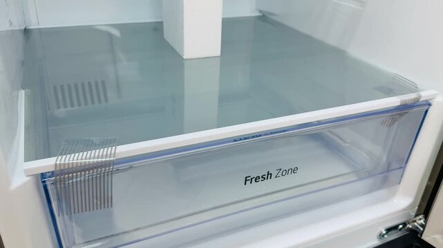 Clean refrigerator vegetable shelf with transparent crisper drawer, glass shelf, cool blue LED, spotless white interior, visible.