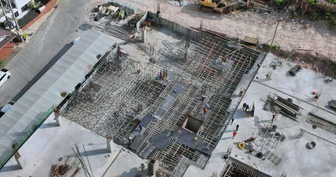 aerial of a massive construction site revealing unidentified workers installing an intricate steel rebar lattice over a reinforced concrete foundation.