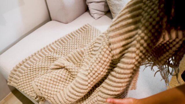 Person Folding a Beige Woven Textured Rug on a White Sofa