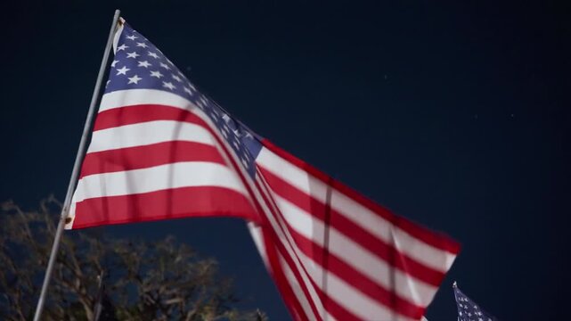 American flag close view illuminated at night in Malibu, California, USA, fabric moving in wind under strong light creating dramatic patriotic memorial atmosphere