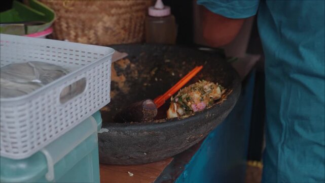 Traditional Indonesian lotek being prepared and served at a street food stall in Bandung, Indonesia. Fresh vegetables mixed with peanut sauce and enjoyed as a local culinary experience in an authentic