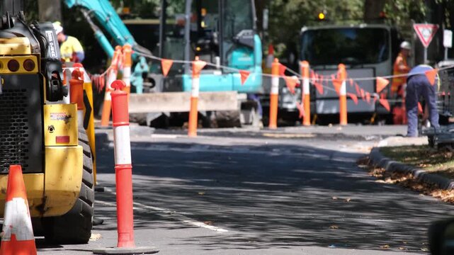 Close-up of construction machinery at a roadworks site in Australia, with workers and activity blurred in the background. Infrastructure maintenance, equipment, safety, working crew and urban repair 