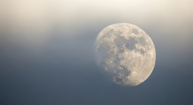 Immense pearlescent super moon peeking from behind atmospheric haze during a night sky observation