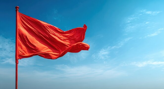 Fractured red flag made of lightweight fabric with a textured surface, waving vigorously in the wind against a bright blue sky with scattered clouds