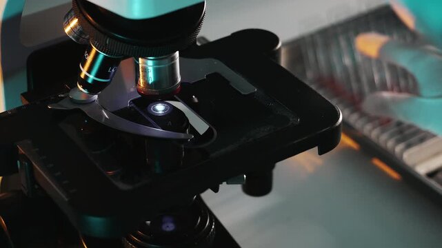 Close up of lab technician replacing glass slide under microscope during scientific analysis and sample preparation in laboratory environment.