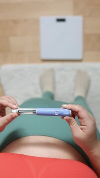 A vertical close up shot. A young woman primes the pen injector, preperes it for injection
A young woman primes pre-filled pen injector with semaglutide on floor and scales background