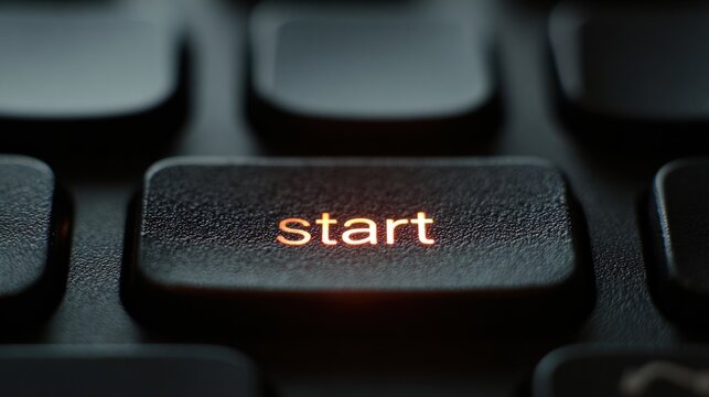 A black computer keyboard with an illuminated orange 'start' button, highlighting a sleek textured surface and modern design