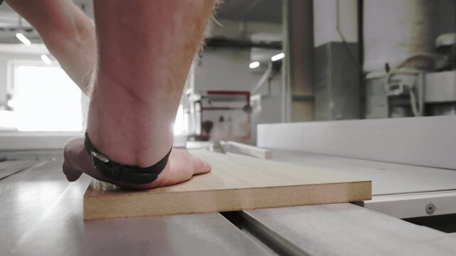 Close up of worker pushing wooden board through table saw during cutting process in woodworking workshop and furniture production.