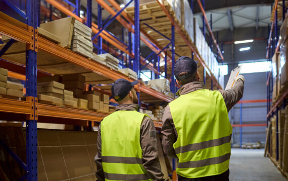 Warehouse workers perform inventory stocktaking with clipboard. They coordinate storage, check boxes and plan shipping in a modern facility. Reliable teamwork and stock control concept.