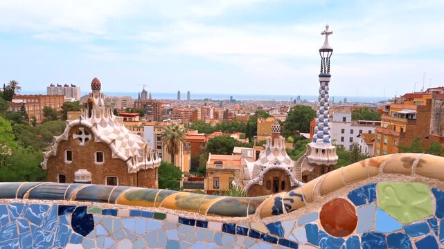 Gaudi's park guell mosaic bench offers panoramic barcelona skyline view under blue sky.