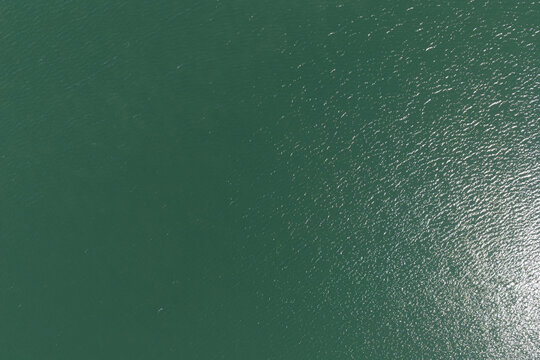 Green water surface aerial view showing ripples and sunlight reflecting on the aquatic texture