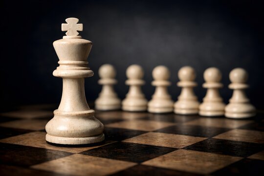 White chess king stands prominently in the foreground on a vintage chessboard, asserting leadership over an array of pawns.
