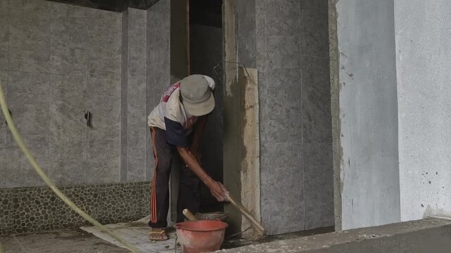 A worker spreads and smooths cement on a wall surface as part of the finishing process