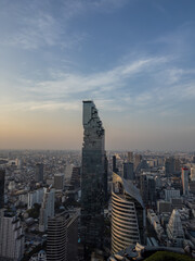 Fototapeta premium A breathtaking panoramic aerial view of Bangkok's sprawling cityscape at dusk, highlighted by the striking architectural marvel of the MahaNakhon Tower. Modern skyscrapers pierce the horizon,
