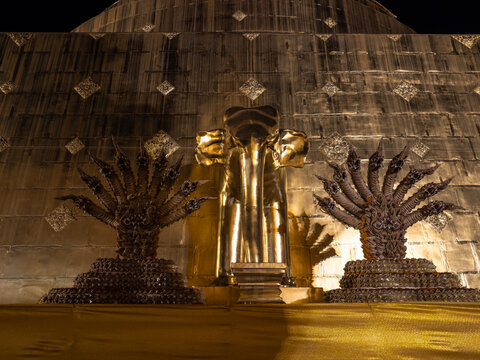 Golden elephant statue flanked by multi-headed Naga serpents against a shimmering gold temple wall at Wat Saket, Bangkok. Evoking ancient Thai spirituality and architectural grandeur at night.