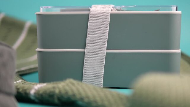 Double layer green bento box with white elastic strap sitting on a table with green fabric.