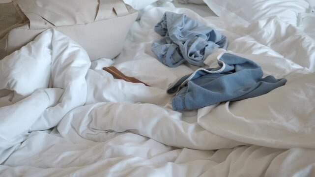 Messy unmade bed with blue pajamas and rumpled white sheets in morning sunlight at home.