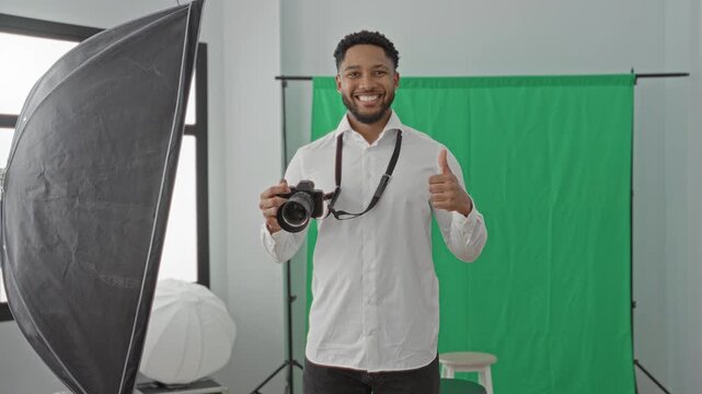 Man holding camera with strap and giving thumbs up in studio with green screen and lighting; confidence.