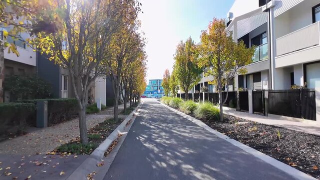 Tree-lined residential street in a modern suburban neighborhood in Melbourne, Australia, with townhouses and landscaped verges. Urban planning, housing, and comfortable living environment.