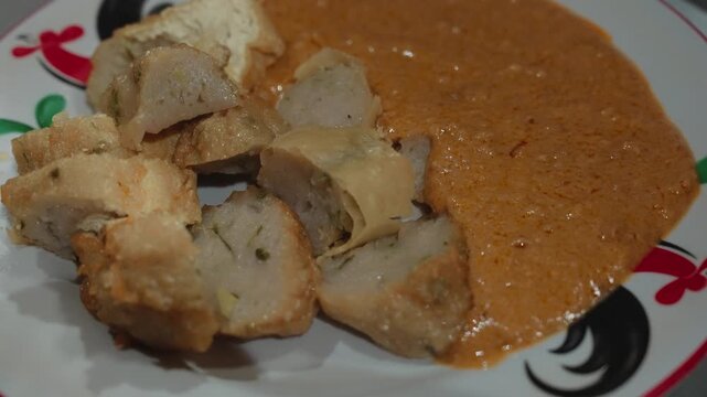 Traditional Indonesian batagor being fried, prepared, served with peanut sauce, and eaten at a local street food stall in Bandung. Authentic culinary scene showcasing popular West Java snack culture