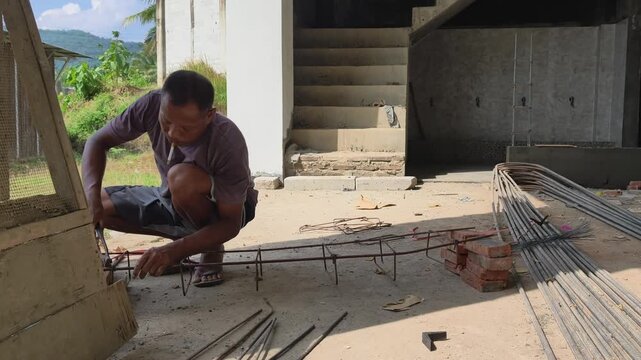 Construction worker tying iron rings for beam reinforcement while smoking a cigarette
