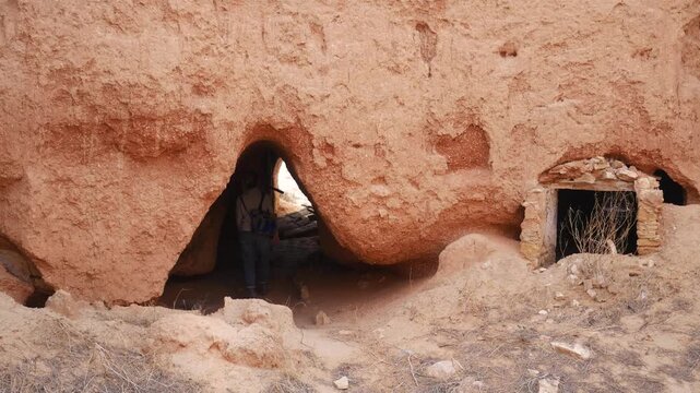 Tourist visiting traditional troglodyte cave dwelling in Matmata, Tunisia. Historic underground Berber architecture carved into desert rock landscape.