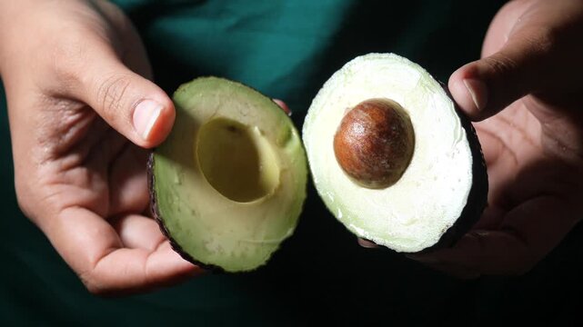 Close up video of hands holding two halves of a fresh avocado fruit in dynamic motion.