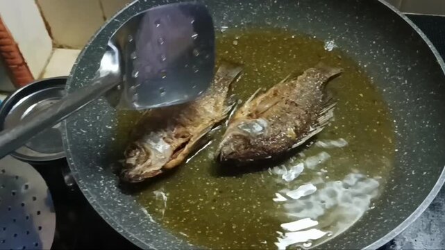 Whole tilapia fish are being fried in a pan filled with hot oil on the stove