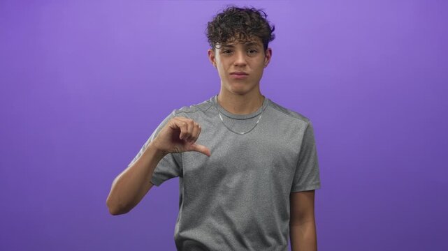 Man displays thumb down gesture with bare hand and silver chain in studio purple backdrop; youth disapproval.