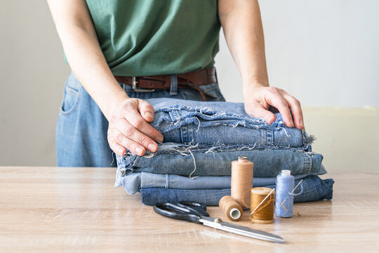 Person preparing upcycled denim fabric, thread, and scissors for sewing. Creative craft hobby saving the environment, upcycling denim jeans reusing old clothes. Reusing things