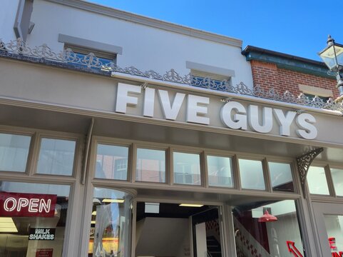 London, UK 03.07.2025 fast food restaurant facade with five guys sign on building exterior under blue sky urban street scene with open neon sign and takeaway interior visible