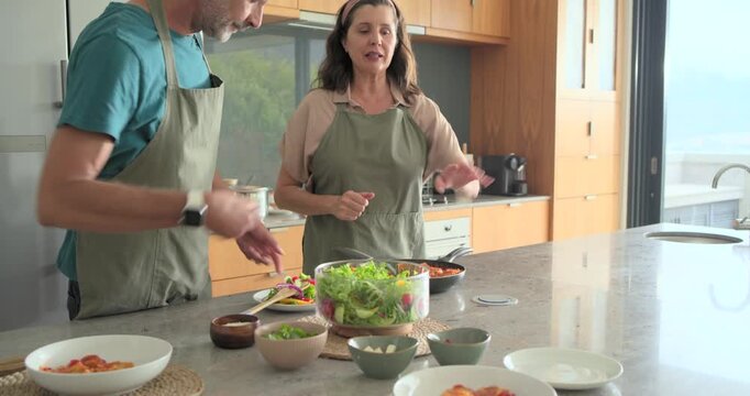 Noticing glass salad bowl, Diverse couple in aprons tossing salad with wooden servers at island