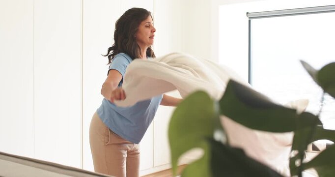 Couple with mature woman making bed after lifting white sheet, smoothing it in bedroom, copy space