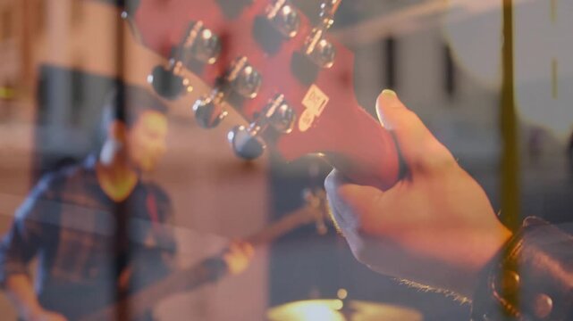 Guitarist tuning guitar and plucking in music rehearsal flare growing camera widening showing band