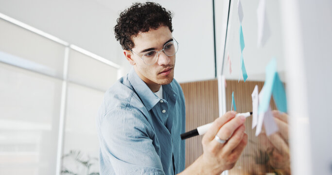 Man, writing or planning with glass board in office for schedule, tasks or project agenda. Male person, employee or brainstorming with sticky note or marker for reminder, ideas or work strategy